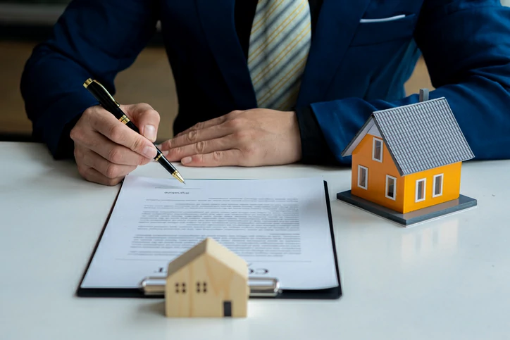 Homme signant un document à côté d'une maquette de maison.