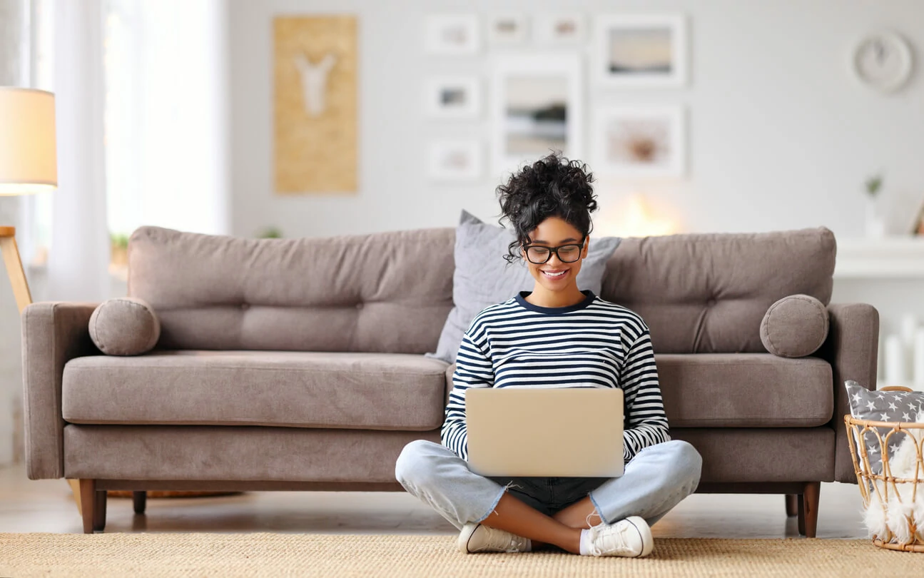 Jeune femme noire utilisant un ordinateur portable et assise en bas d'un canapé