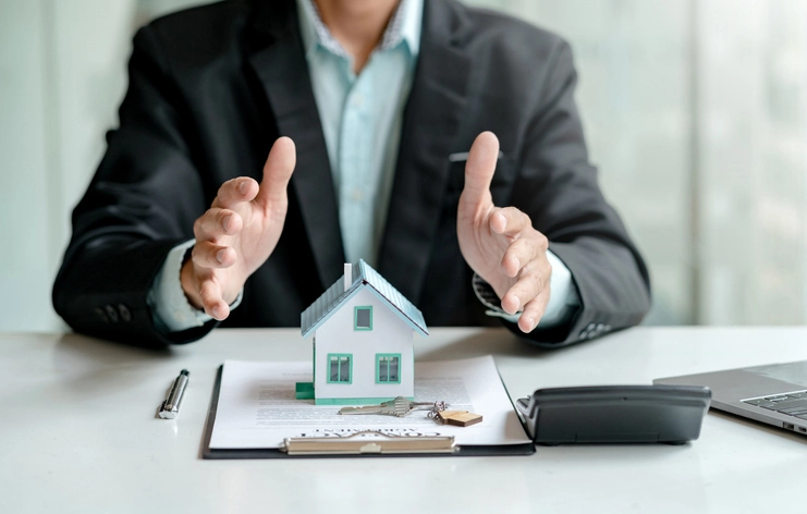 Homme qui tend ses mains au-dessus d'une petite maison et des documents.