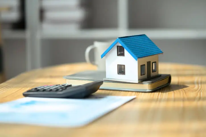 Petite maison posée sur un agenda, un document et une calculatrice.