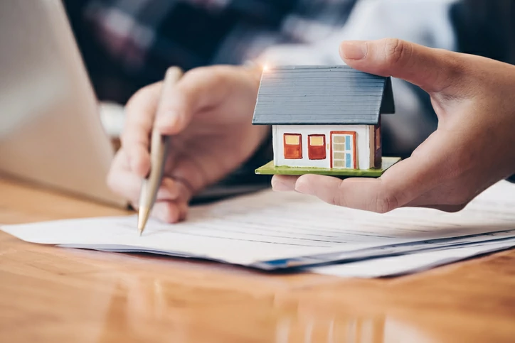 Homme signant un document tout en tenant une petite maison