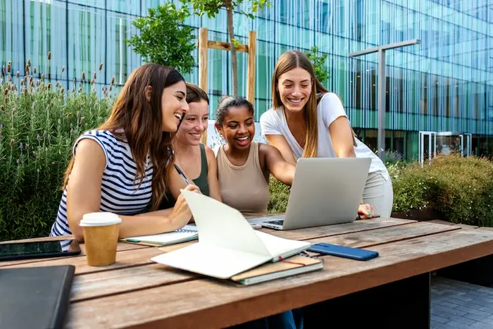 Quatre jeunes femmes en train de consulter des documents devant un ordinateur portable.