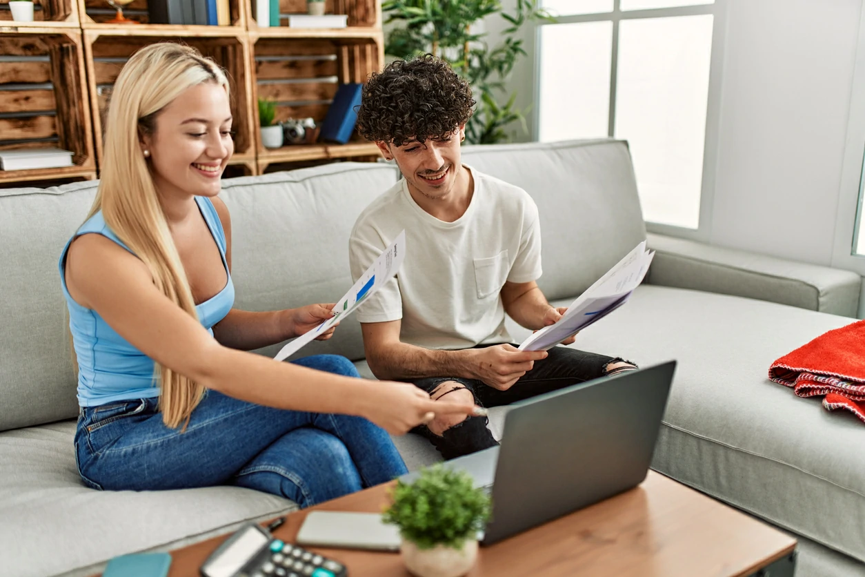 Deux étudiants qui consultent l'écran d'un ordinateur portable avec des cahiers à la main.