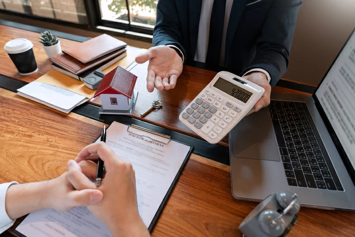 Homme qui tient une calculatrice devant un autre homme qui s'apprête à signer un document.