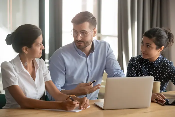 Trois personnes qui discutent autour de documents et d'ordinateur portable.
