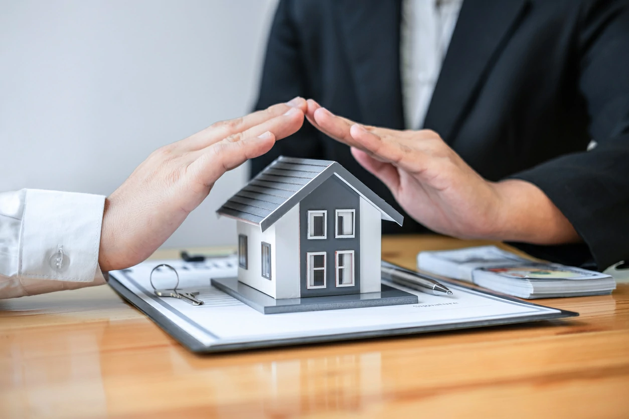 Deux mains qui couvrent une maquette de maison au dessus d'un document.