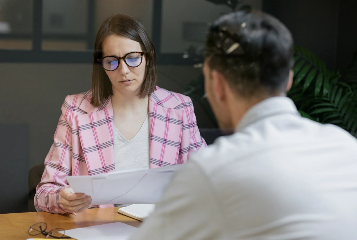 Femme consultant des documents en face d'un homme sur son bureau.